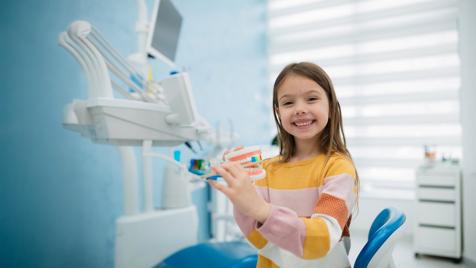 Smiling girl holding a dental model at the dentist